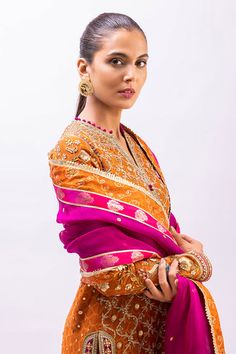 This marori work orange cotton net kurta has bright pops of fuschia pink and turquoise detailings. It is paired with a bright pink brocade shalwar detailed with zardoze and a kamdani organza dupatta. Pink Katan Silk Kurta With Traditional Drape, Pink Katan Silk Kurta With Zari Work, Pink Anarkali Unstitched Suit With Dabka Detail, Pink Anarkali Unstitched Suit With Dabka, Designer Katan Silk Kurta With Dupatta, Eid Sheer Dupatta Katan Silk Kurta, Eid Katan Silk Kurta With Sheer Dupatta, Pink Unstitched Suit With Dabka In Traditional Drape, Pink Unstitched Suit With Dupatta In Raw Silk