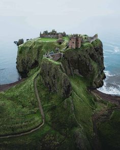 an old castle sits on top of a cliff by the ocean, surrounded by lush green grass