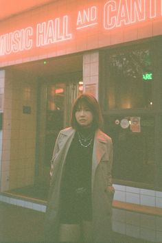 a woman standing in front of a music hall and can't store with the neon sign above her