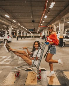 two women are sitting in a shopping cart and one is standing up with her legs spread out