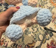 a hand holding a small teddy bear on top of a carpeted floor next to a rug