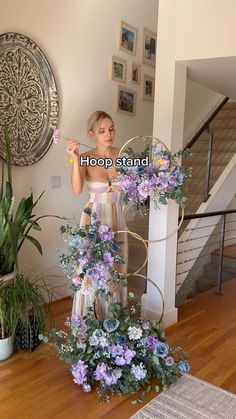 a woman standing in front of a flower arrangement on top of a wooden floor next to a stair case