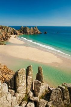 the beach is surrounded by large rocks and blue water