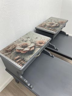 two metal trays with flowers painted on them sitting side by side in a corner