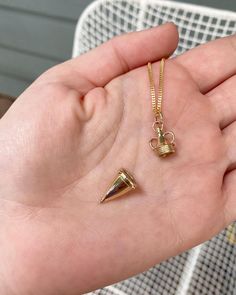 a hand holding a gold necklace with two small pendants on it's fingers