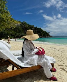 a woman sitting on top of a beach next to the ocean wearing a straw hat