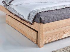 a wooden bed frame with white sheets and grey blankets on it, in front of a rug