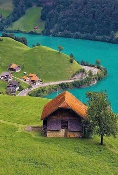 an old wooden house on the side of a hill overlooking a body of blue water