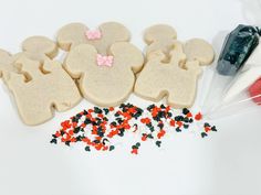 some cookies shaped like mickey and minnie mouses are on a white table with red and black sprinkles