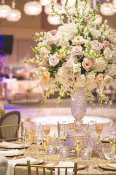 a vase filled with white and pink flowers on top of a table covered in wine glasses