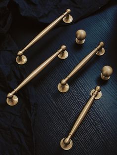 four brass handles and two knobs on a black surface with dark fabric in the background