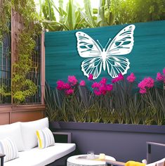 an outdoor seating area with white furniture and purple flowers on the wall, along with a butterfly mural