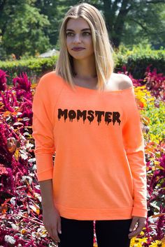 a woman standing in front of flowers wearing an orange sweatshirt with the word monster on it