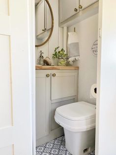 a white toilet sitting inside of a bathroom next to a sink under a round mirror