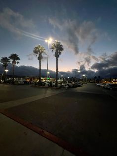 a parking lot with cars parked in it and palm trees on the side of the road