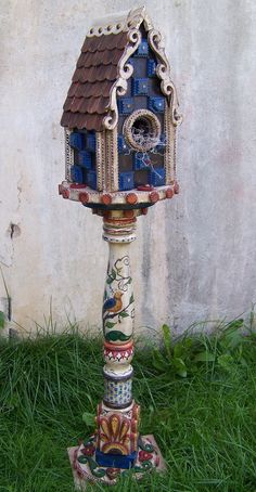 a bird house made out of ceramic tiles on top of a pole in the grass