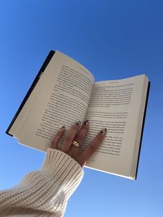 a woman is holding an open book in her hands and looking up into the sky