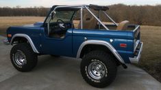 a blue truck parked on top of a cement road next to a field and trees