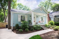 a small blue house with white trim on the front door and porch, along with landscaping