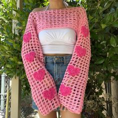 a woman is wearing a pink crocheted cardigan with hearts on the sleeves