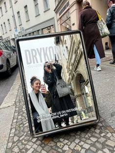 an advertisement for drykor is displayed on the sidewalk in front of some people walking down the street