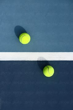 two tennis balls sitting on top of a blue and white court next to each other