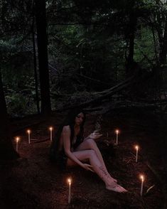 a woman sitting on the ground surrounded by lit candles in the dark forest at night