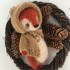 a knitted teddy bear sitting in a wreath with pine cones