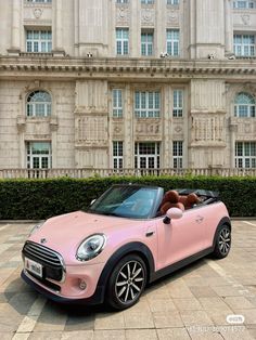 a pink mini convertible parked in front of a large building