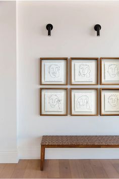 four framed drawings hang on the wall above a bench in a room with hardwood floors