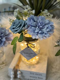 blue flowers are in a mason jar on a white tablecloth with books and lights