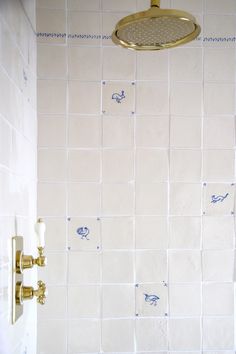 the shower head is gold in color and it has blue tile on the wall behind it