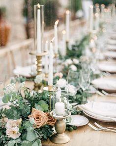 an elegant table setting with candles and greenery on the centerpiece, plates and napkins