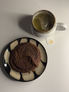 a chocolate cookie on a plate next to a cup of tea