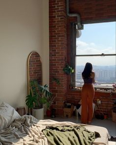 a woman standing in front of a window looking out at the city from her bed