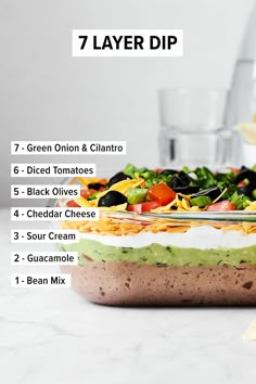 the ingredients for a layered layer dip in a glass dish on a counter top with chips and guacamole