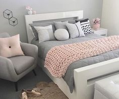 a gray and white bedroom with pink accents on the bed, two grey armchairs