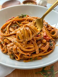 a white bowl filled with pasta and sauce on top of a wooden table next to utensils