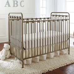 a baby crib with white bedding and pillows on the floor next to a window