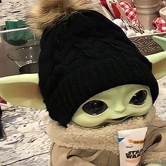 a baby yoda doll wearing a black hat and scarf on top of a table