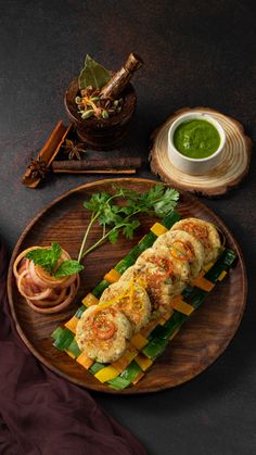 a wooden plate topped with food next to a bowl of sauce and a cup of green tea