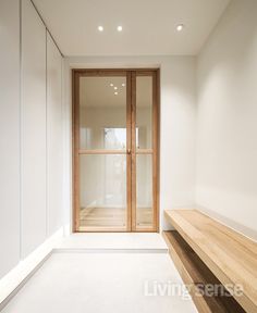 an empty white room with wooden bench and glass doors