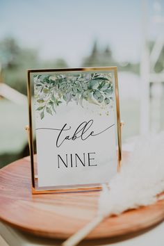 a table name sign sitting on top of a wooden table next to a white feather