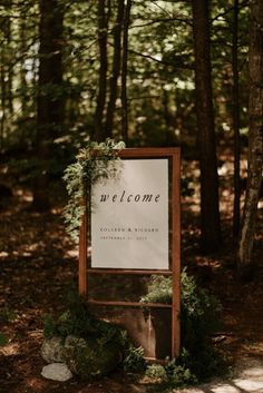 a welcome sign in the woods with greenery