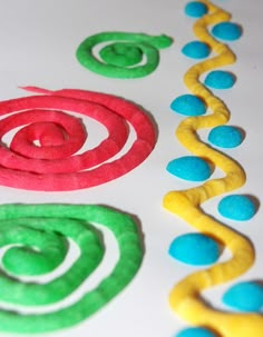 colorful circles and spirals made out of play dough sitting on a table with white surface