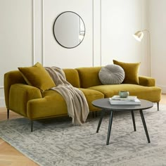 a living room with a yellow couch, round mirror and rug on the floor in front of it