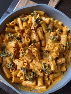 a white bowl filled with pasta and broccoli on top of a wooden table