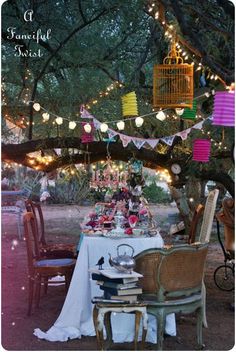 a table set up for a tea party under a tree with lanterns and birdcages