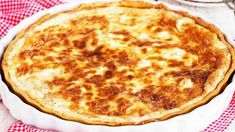 a cheese pizza sitting on top of a white plate next to a red and white checkered table cloth