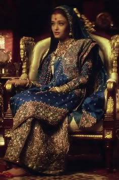 a woman sitting in a chair wearing a blue and gold dress with an elaborate head piece